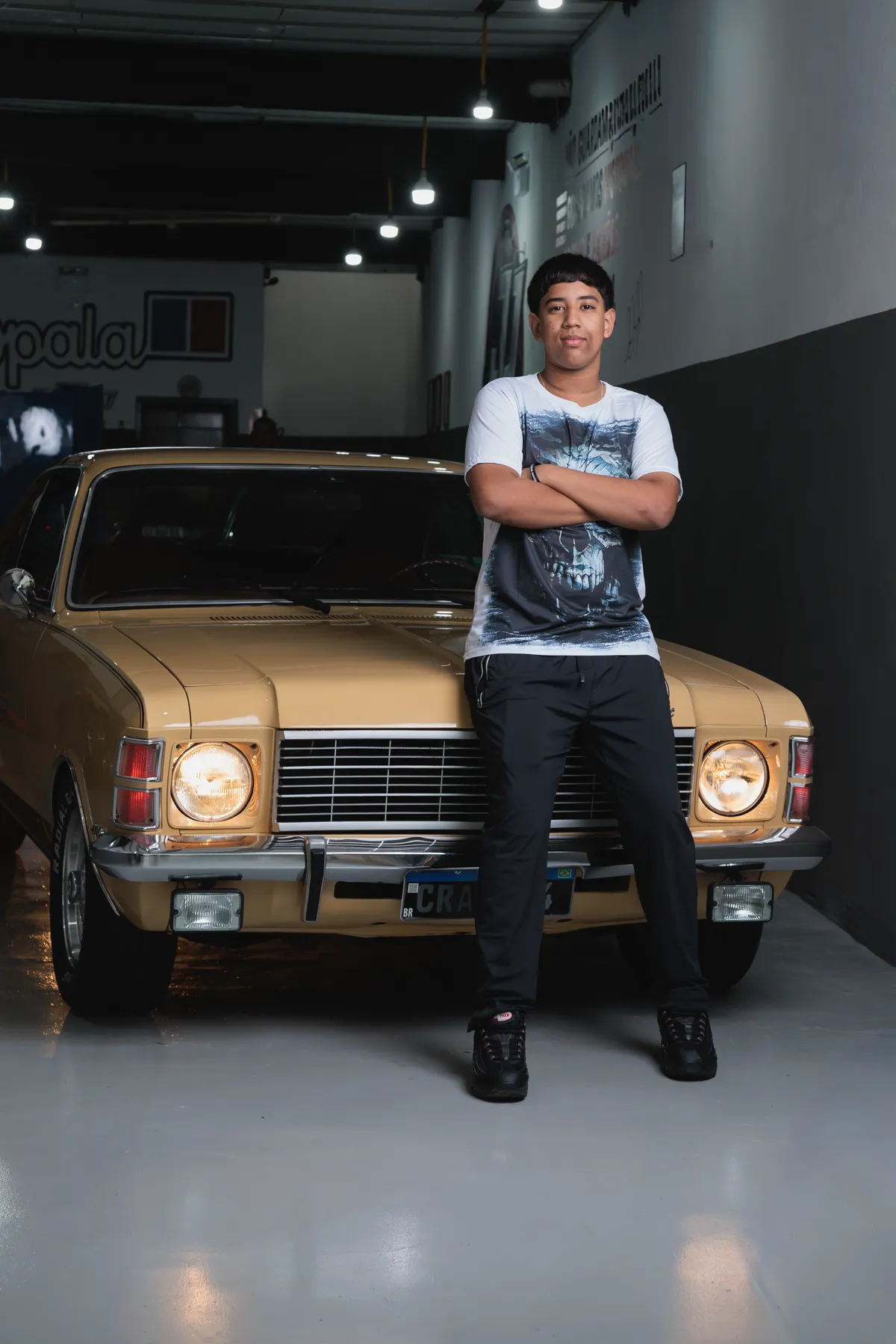 Filho da família encostado no Opala cupê dourado na garagem